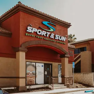 A building with a red exterior, a blue sign that says 'SPORT & SUN', and a glass door with a picture of a woman wearing goggles.