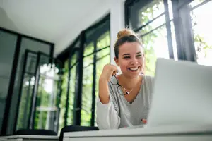 A woman sitting at a desk with a laptop and a window behind her