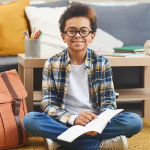 A smiling boy wearing glasses and holding a book in a cozy living room setting
