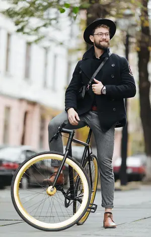 A man wearing a hat and glasses sits on a bicycle in front of a building.