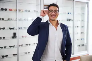A man with glasses smiles while standing in front of a display case with sunglasses