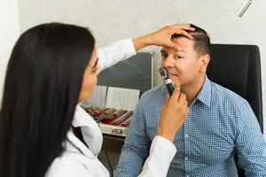 A female doctor examining a male patient's eye using an ophthalmoscope in a medical setting.
