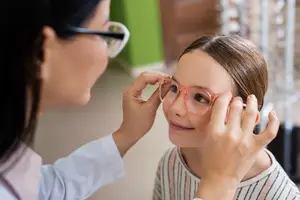 An optician tries on glasses with a young girl in a white lab coat in a store