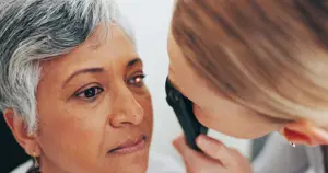 An older woman with gray hair is having her eyes examined by a doctor in a white coat.