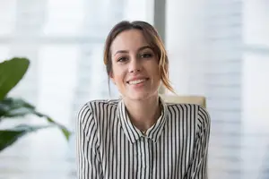 Close-up of a woman with short hair in a striped shirt smiling at the camera in an office setting