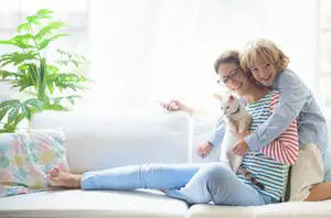 A family sitting on a couch with a cat, smiling and holding a remote control