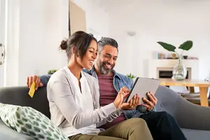 A woman and a man sitting on a couch smiling at a tablet