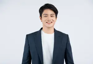 A man wearing a white t-shirt and a navy blue blazer is smiling and posing for a photo