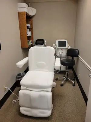 A white leather recliner chair is in a room with beige walls, a trash can, a wooden shelf, and a black chair.