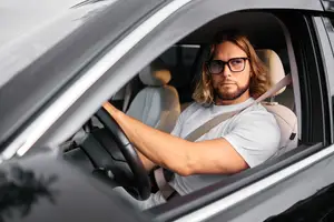 A man wearing glasses is driving a car on the road