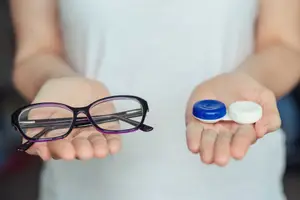 Woman holding glasses and contact lenses