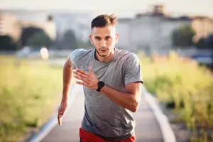 A man running outdoors in a gray t-shirt and red shorts with a black smartwatch on his wrist.