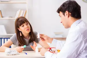 A woman is sitting on a chair and talking to a man in a white shirt in an office room.