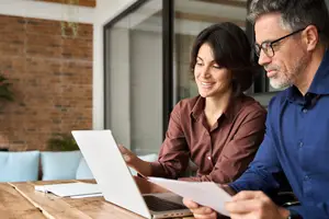 A man and woman working together at a table, looking at a laptop screen