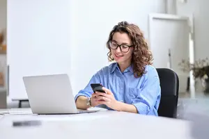 woman smiling looking at her phone while sitting at her desk
