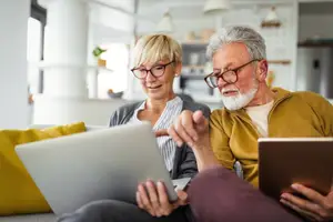 An elderly couple using a laptop and tablet computer in their living room