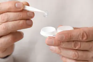 A person is holding a contact lens and a contact lens case in their hands.