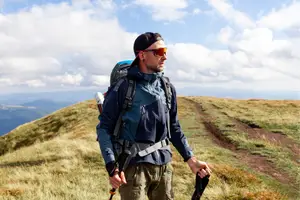 A man hiking in a mountain with a clear sky and clouds in the background