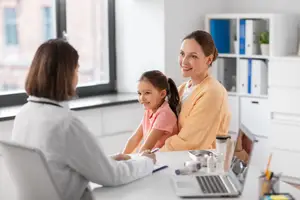 A doctor consults with a mother and her young daughter in a doctor's office.