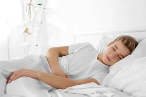 A teenage boy sleeping peacefully in a white bed with a white pillow and white blanket