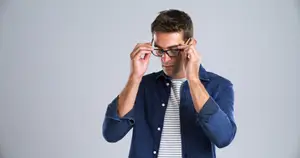 A man in a blue shirt adjusting his glasses while holding a pencil