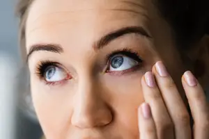 A woman with blue eyes applying eye drops