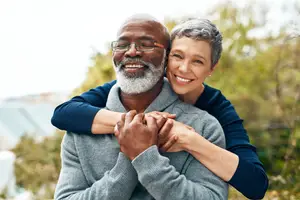 A smiling couple embracing each other in a park with trees in the background
