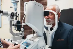 An elderly man is sitting in front of an eye examination machine in a clinic.