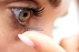 Close-up of a woman's hand placing a contact lens in her eye.