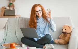 A girl sitting on a couch using a laptop and showing a peace sign