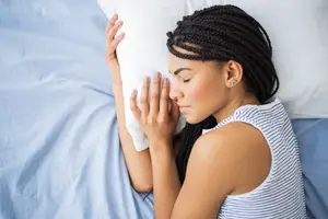 A woman is sleeping on a bed while holding a white pillow