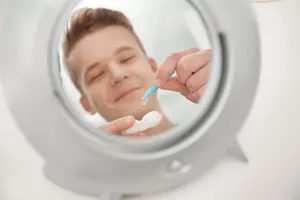 A man looking in a mirror and putting in contact lenses