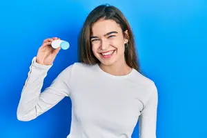 A woman smiling and holding a bottle of eye drops in her hand