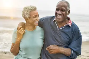 A happy elderly couple smiling on the beach with the ocean in the background
