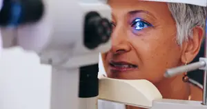 A woman with gray hair is having her eyes examined using a medical device with a blue light.