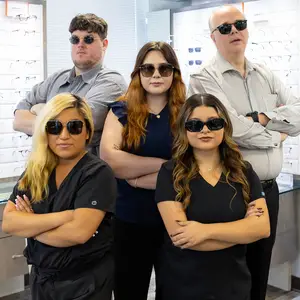 Five people in sunglasses pose for a photo in a room with glass walls displaying sunglasses