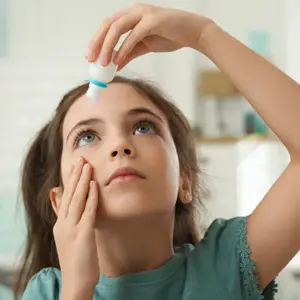 A young girl is administering eye drops to her eye.