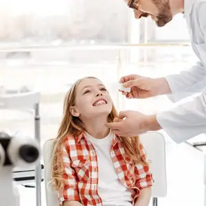 A man in a white lab coat is checking a child's eye with a penlight.