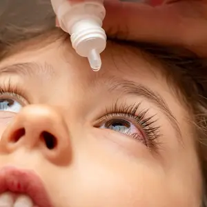 A young girl has an eyedropper held by another person to her eye