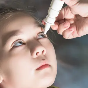 A person administering eye drops to a child