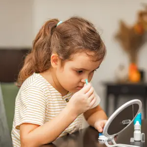 A girl uses eye drops while sitting at a table in front of a mirror