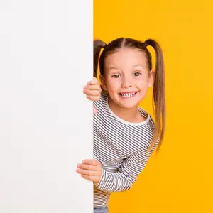 A smiling girl with pigtails holding a white board in front of a yellow background