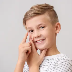 Young boy with a short haircut and smiling while putting in a contact lens