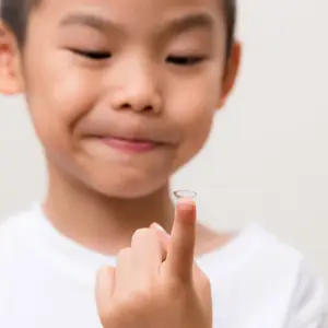 A boy holding a contact lens in his right hand and smiling for the camera.