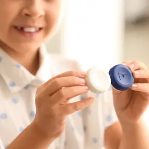 A young girl with a smiling face is holding a white and blue object in both hands and seems to be posing for a photo.