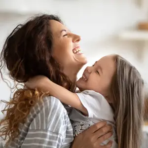 A woman and a young girl are smiling and hugging each other in a room