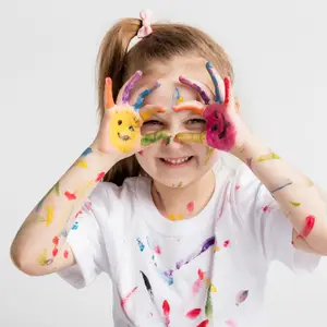 A young girl with colorful paint on her hands and face, smiling and posing for a picture.