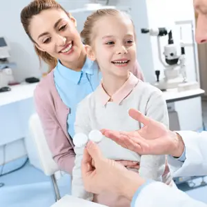 A doctor showing a girl and her mother two white contact lenses