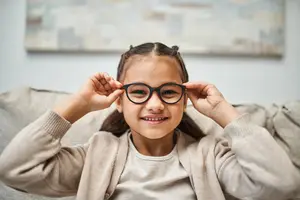 A young girl is smiling while wearing glasses and holding them up to her eyes.