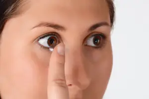 A woman is trying to insert a contact lens into her eye.